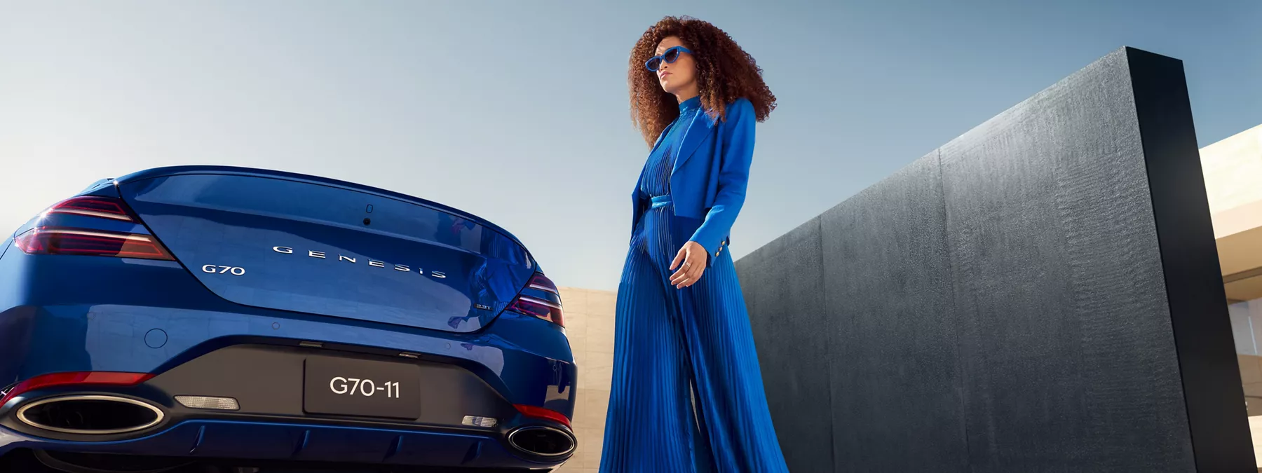 Exterior Rear View Of Genesis G70 In Kawah Blue As Woman Dressed In Blue